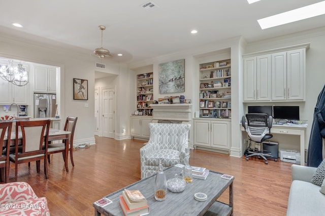 living room featuring a chandelier, light wood-type flooring, built in shelves, and ornamental molding