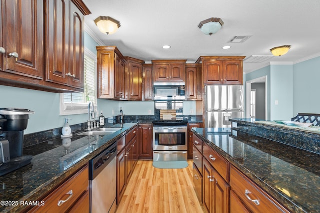 kitchen with sink, ornamental molding, appliances with stainless steel finishes, dark stone counters, and light hardwood / wood-style floors