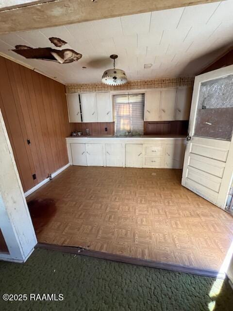 kitchen with hanging light fixtures, white cabinets, light parquet floors, and wood walls