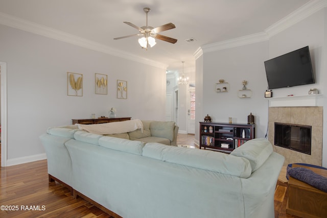 living room featuring a tiled fireplace, crown molding, ceiling fan with notable chandelier, and hardwood / wood-style floors