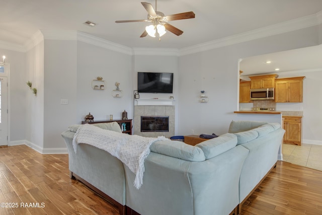 living room featuring ornamental molding, ceiling fan with notable chandelier, a fireplace, and light hardwood / wood-style flooring