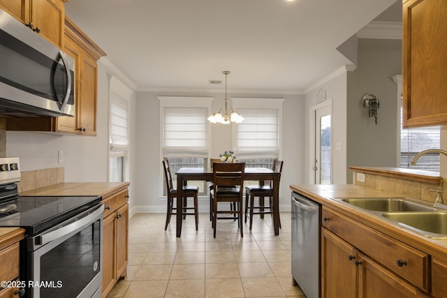 kitchen with sink, crown molding, appliances with stainless steel finishes, light tile patterned flooring, and decorative light fixtures