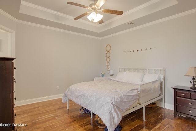 bedroom featuring hardwood / wood-style floors, ornamental molding, a raised ceiling, and ceiling fan