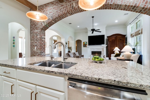 kitchen with light stone countertops, ceiling fan, pendant lighting, sink, and stainless steel dishwasher