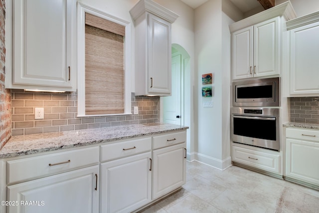 kitchen featuring light stone counters, stainless steel appliances, white cabinets, and decorative backsplash