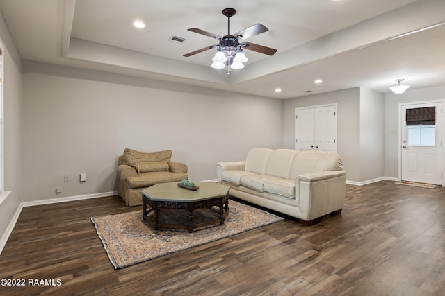 living room with ceiling fan, dark wood-type flooring, and a tray ceiling