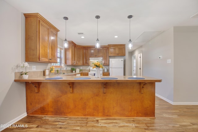 kitchen featuring sink, kitchen peninsula, white fridge, and hanging light fixtures