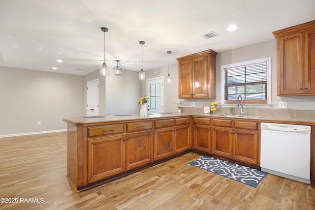 kitchen featuring dishwasher, light wood-type flooring, decorative light fixtures, sink, and kitchen peninsula