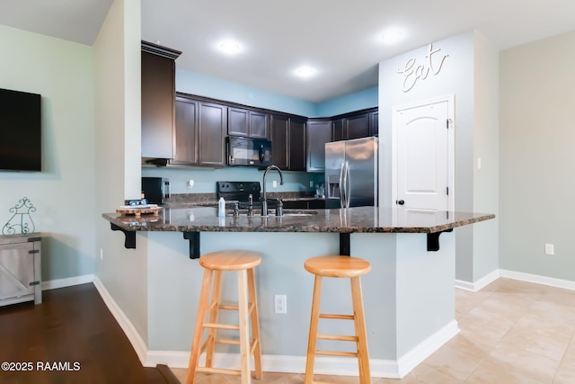 kitchen featuring a kitchen breakfast bar, sink, dark stone counters, and stainless steel fridge with ice dispenser