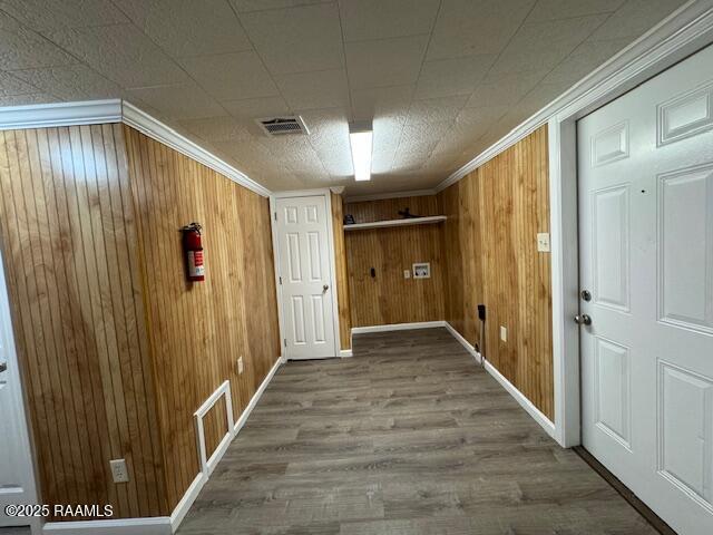 clothes washing area with ornamental molding, wood-type flooring, and wooden walls