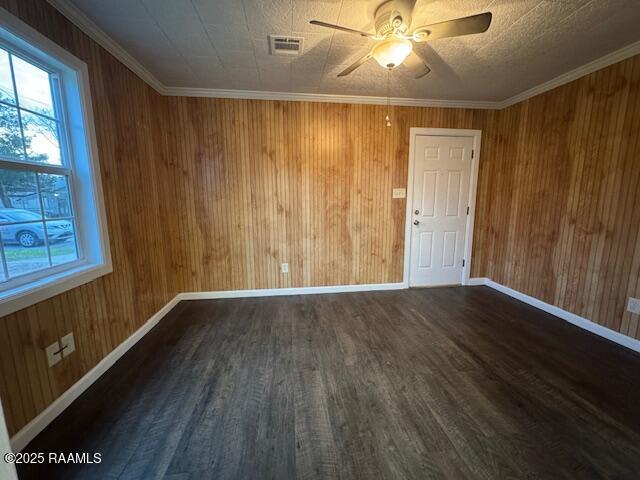 spare room with wooden walls, ceiling fan, dark wood-type flooring, a textured ceiling, and ornamental molding