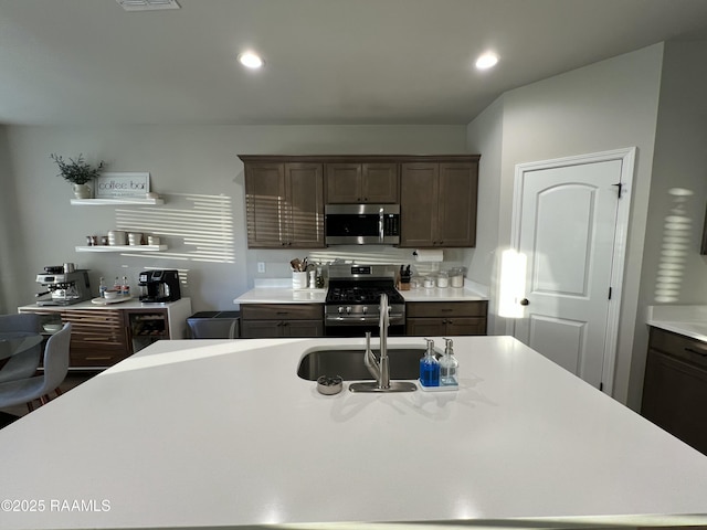 kitchen with a kitchen island with sink, appliances with stainless steel finishes, sink, and dark brown cabinets