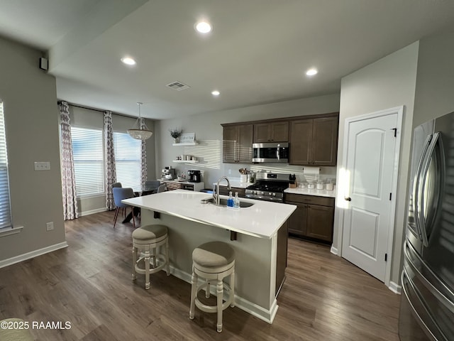 kitchen with decorative light fixtures, a center island with sink, a breakfast bar, sink, and appliances with stainless steel finishes