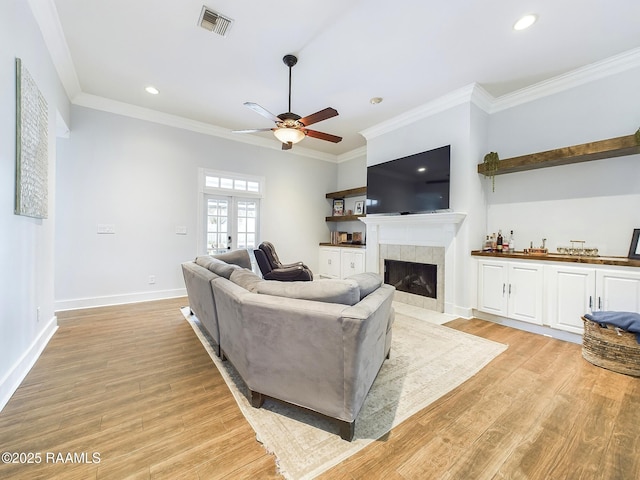 living room featuring french doors, crown molding, light hardwood / wood-style flooring, ceiling fan, and a tiled fireplace