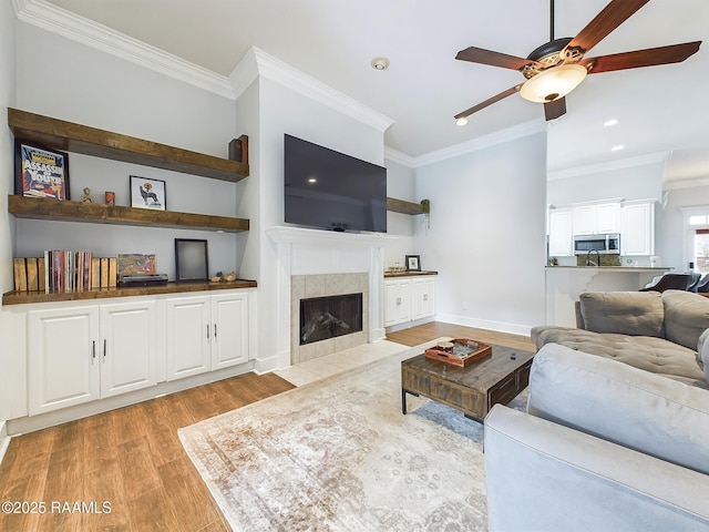 living room featuring crown molding, light hardwood / wood-style floors, a tile fireplace, and ceiling fan