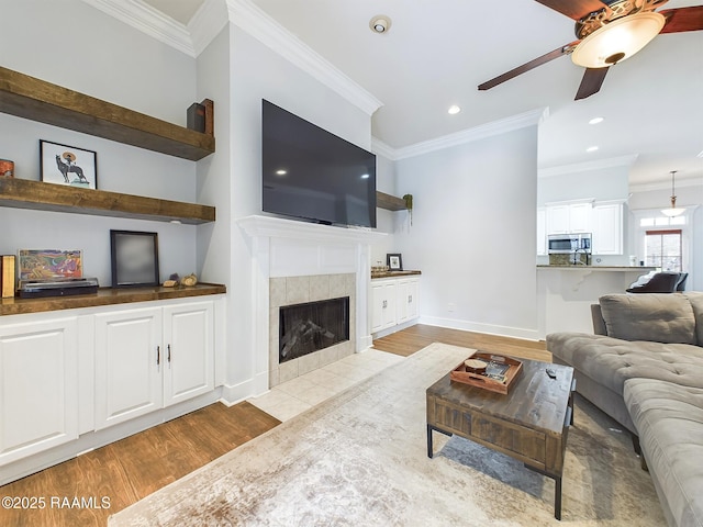 living room with ceiling fan, ornamental molding, a tile fireplace, and light hardwood / wood-style flooring