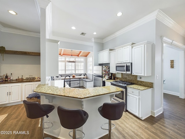 kitchen featuring white cabinetry, a kitchen bar, hardwood / wood-style flooring, stainless steel appliances, and light stone countertops