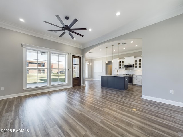 unfurnished living room featuring crown molding, sink, ceiling fan with notable chandelier, and dark wood-type flooring