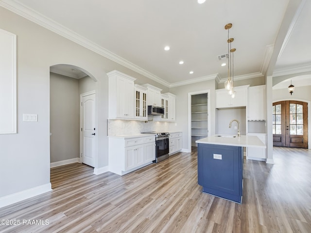 kitchen with stainless steel appliances, white cabinetry, a kitchen island with sink, and decorative light fixtures