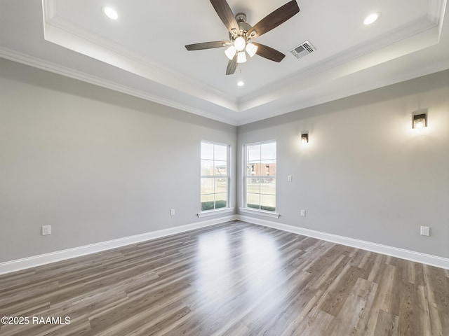 empty room with wood-type flooring, ceiling fan, crown molding, and a tray ceiling