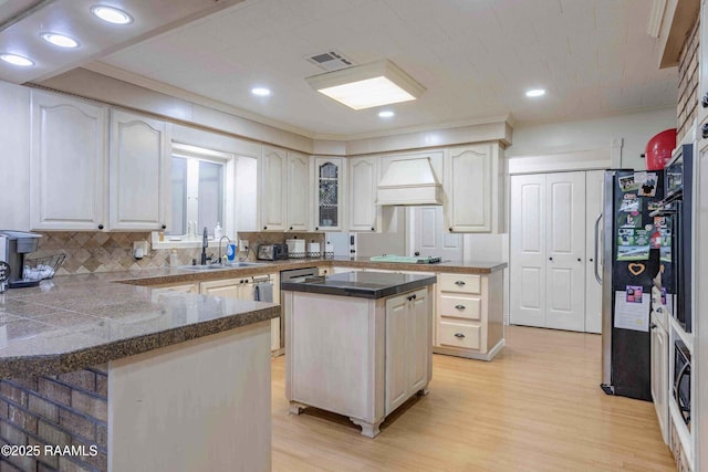 kitchen featuring custom exhaust hood, stainless steel fridge with ice dispenser, a center island, kitchen peninsula, and light hardwood / wood-style flooring