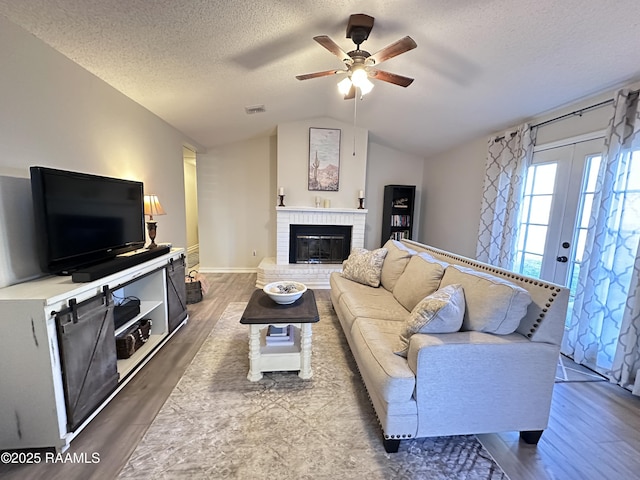 living room with lofted ceiling, a brick fireplace, a textured ceiling, and hardwood / wood-style floors