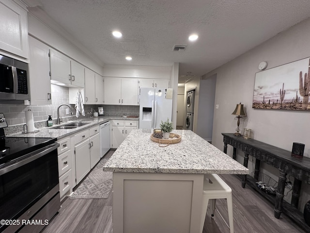 kitchen with stacked washer and dryer, stainless steel appliances, sink, a textured ceiling, and a center island