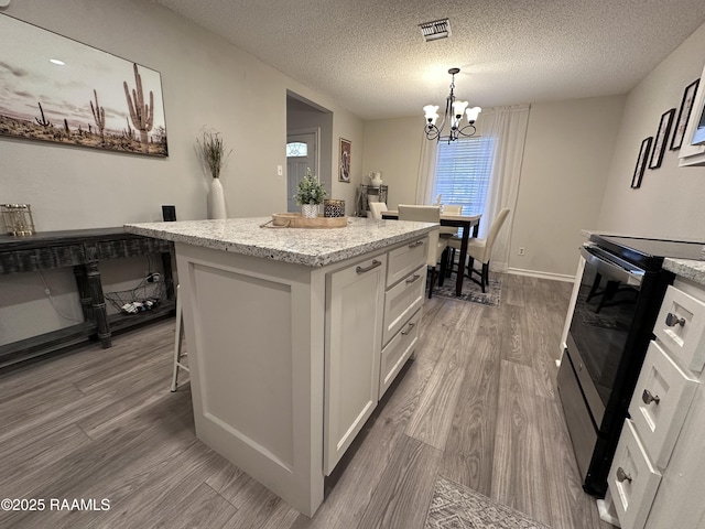 kitchen featuring a kitchen island, wood-type flooring, white cabinetry, an inviting chandelier, and range with electric cooktop