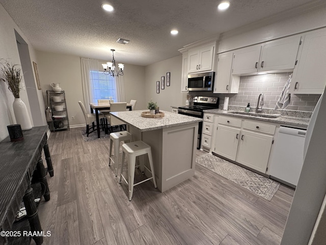 kitchen featuring stainless steel appliances, a center island, a chandelier, white cabinets, and sink