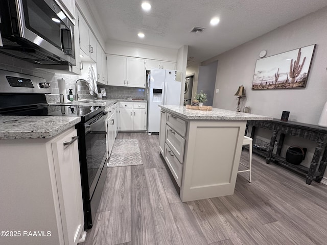 kitchen featuring a textured ceiling, appliances with stainless steel finishes, a kitchen island, white cabinetry, and backsplash