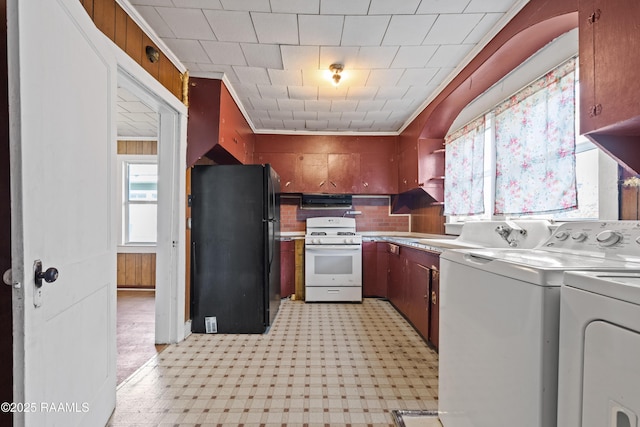 kitchen with washing machine and clothes dryer, gas range gas stove, crown molding, ventilation hood, and black refrigerator