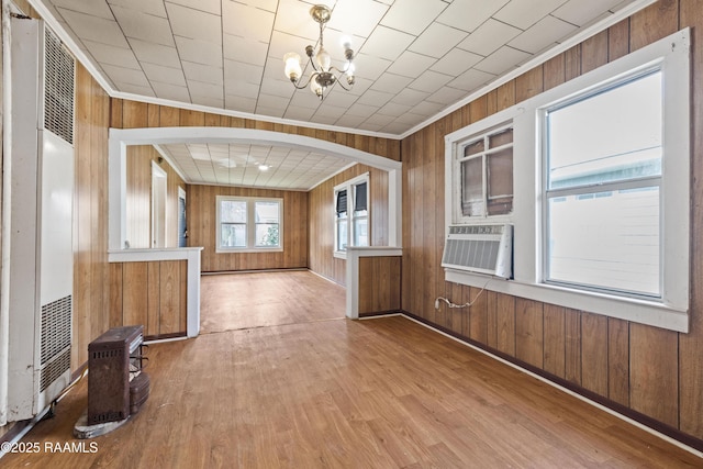 unfurnished living room featuring ornamental molding, wooden walls, a chandelier, and light hardwood / wood-style flooring