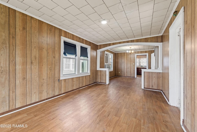 unfurnished living room featuring a notable chandelier, wooden walls, and light hardwood / wood-style floors