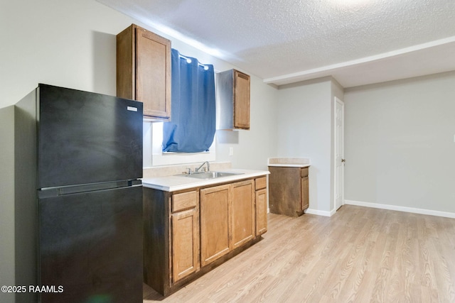 kitchen with light wood-type flooring, sink, a textured ceiling, and black fridge