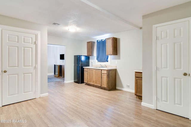 kitchen with a textured ceiling, light hardwood / wood-style floors, black refrigerator, and sink