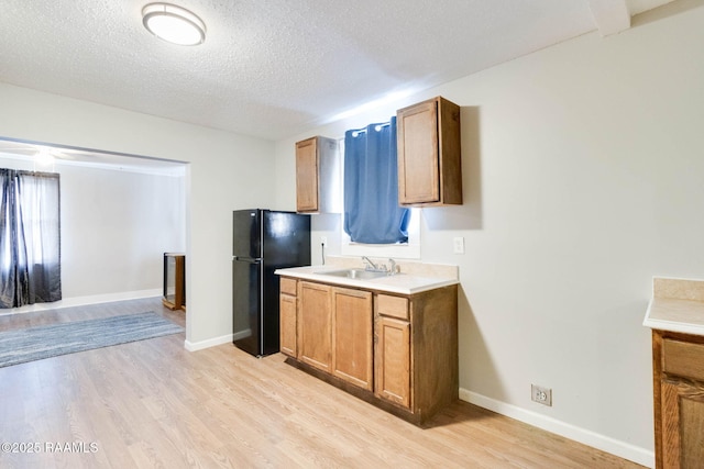 kitchen featuring black fridge, a textured ceiling, light hardwood / wood-style flooring, and sink