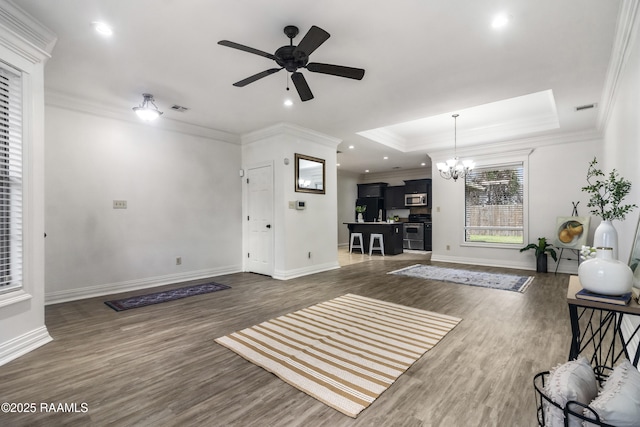 living room featuring ceiling fan with notable chandelier, dark wood-type flooring, a raised ceiling, and ornamental molding