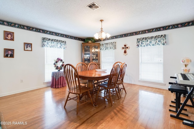 dining space featuring a textured ceiling, light wood-type flooring, and a notable chandelier