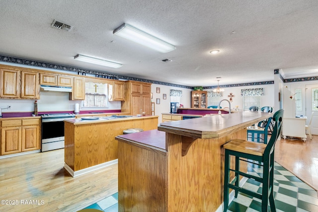 kitchen with a textured ceiling, stainless steel electric range, a kitchen bar, and a kitchen island