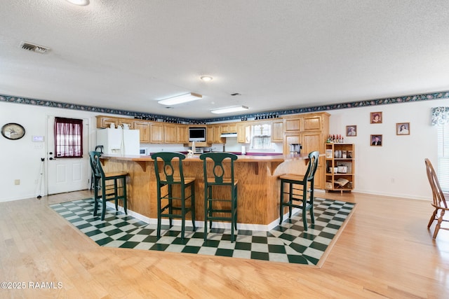 kitchen featuring a textured ceiling, a breakfast bar, light hardwood / wood-style floors, and a spacious island