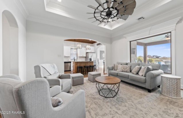 living room featuring ceiling fan with notable chandelier, a raised ceiling, crown molding, and a healthy amount of sunlight