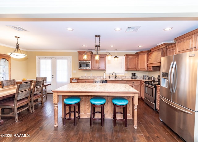 kitchen with pendant lighting, appliances with stainless steel finishes, a center island, custom range hood, and french doors