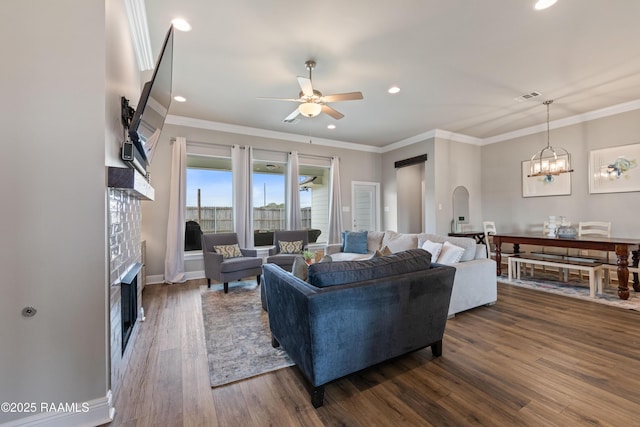 living room with ceiling fan with notable chandelier, ornamental molding, and dark hardwood / wood-style flooring