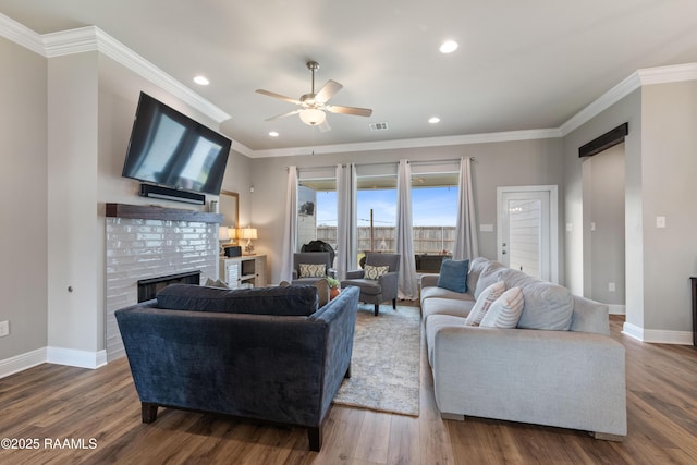 living room with wood-type flooring, a brick fireplace, ceiling fan, and ornamental molding