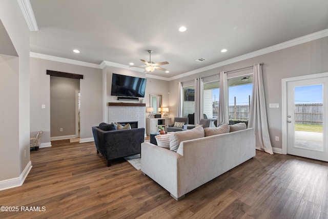 living room with ceiling fan, dark hardwood / wood-style flooring, a brick fireplace, and crown molding