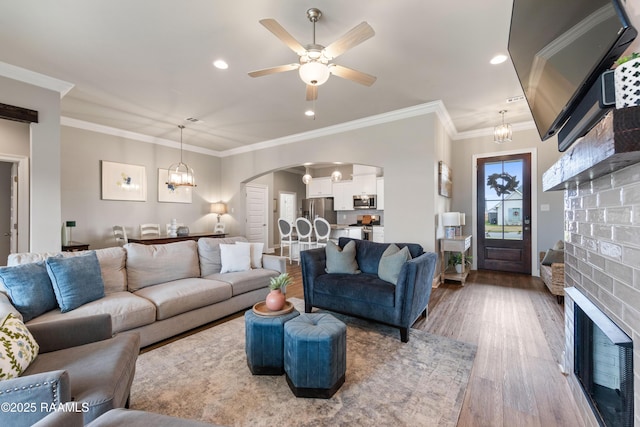 living room with ceiling fan with notable chandelier, a brick fireplace, ornamental molding, and hardwood / wood-style flooring