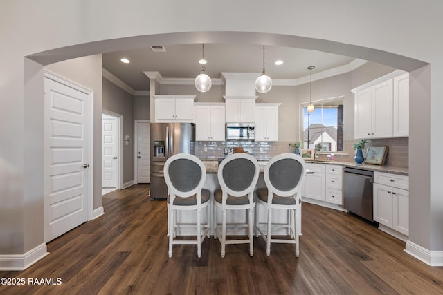 kitchen with stainless steel appliances, white cabinets, a center island, decorative backsplash, and hanging light fixtures