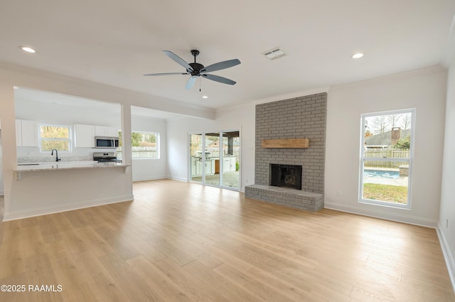 unfurnished living room with sink, light hardwood / wood-style flooring, ornamental molding, ceiling fan, and a fireplace