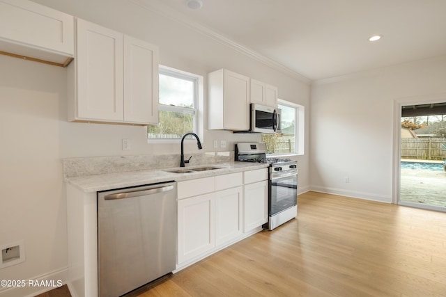 kitchen with sink, white cabinetry, ornamental molding, appliances with stainless steel finishes, and light hardwood / wood-style floors