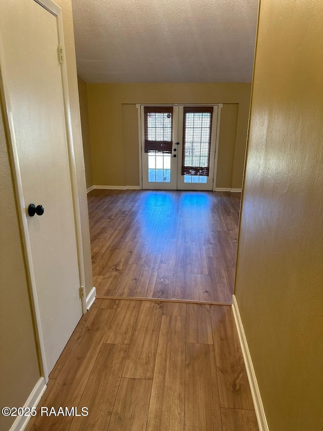 corridor featuring light wood-type flooring, a textured ceiling, and french doors